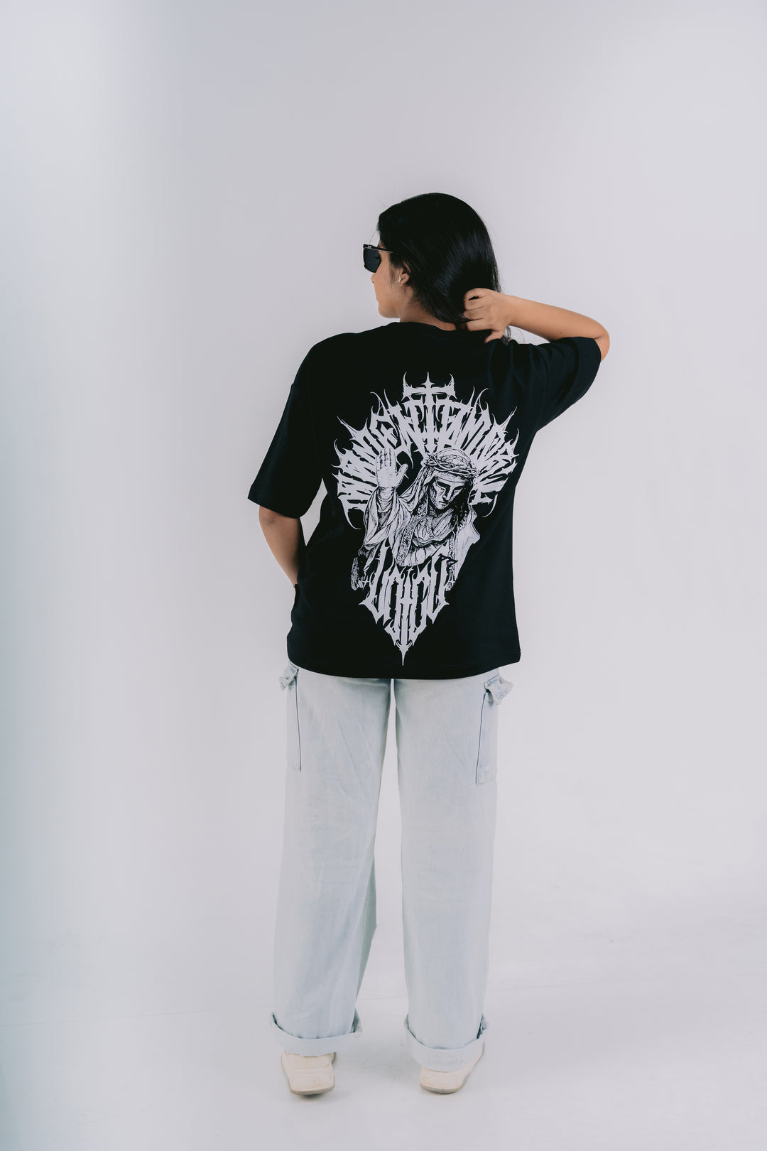 A person shown from the back wearing a black graphic t-shirt with a large white skull design and the text 'BURN THE BONES', paired with light wash jeans and white sneakers, set against a plain light gray studio background.